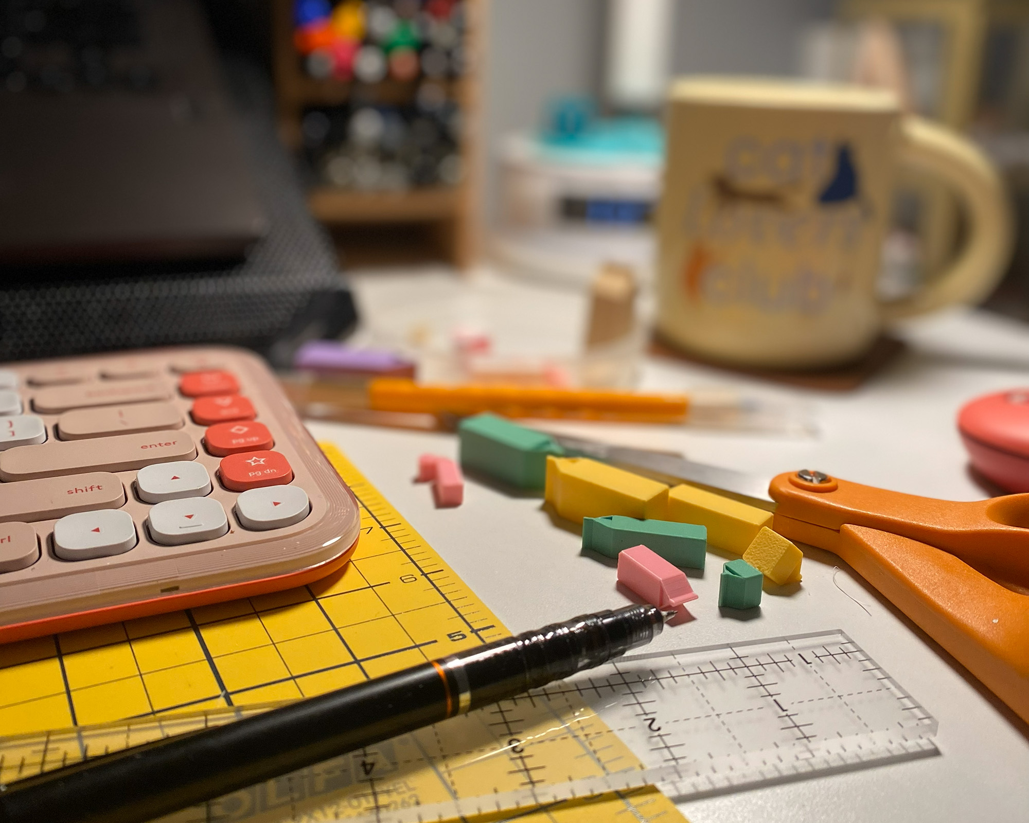 close up view of a white desk with a pencil, ruler, pink keyboard, coffee cup and 3d printed miniature models