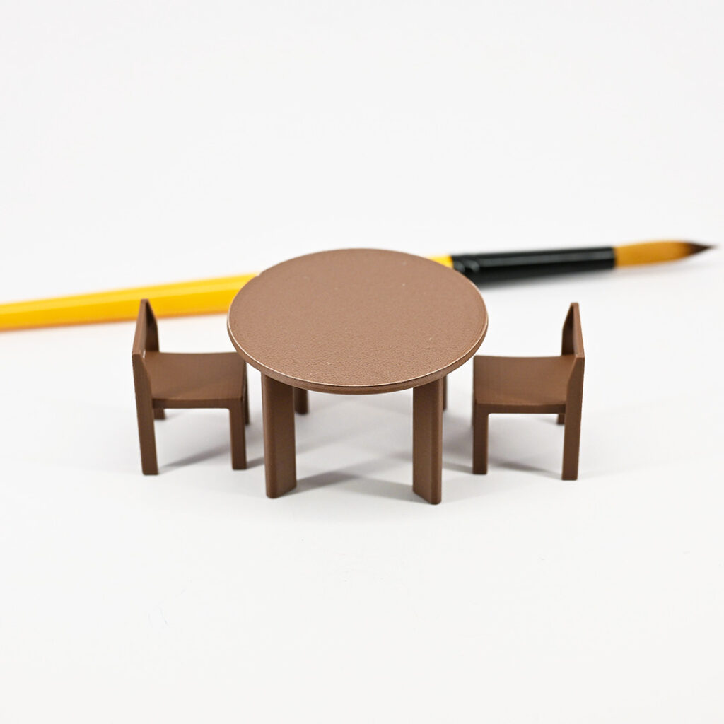 A tiny dining table and two chairs besides a regular size paint brush