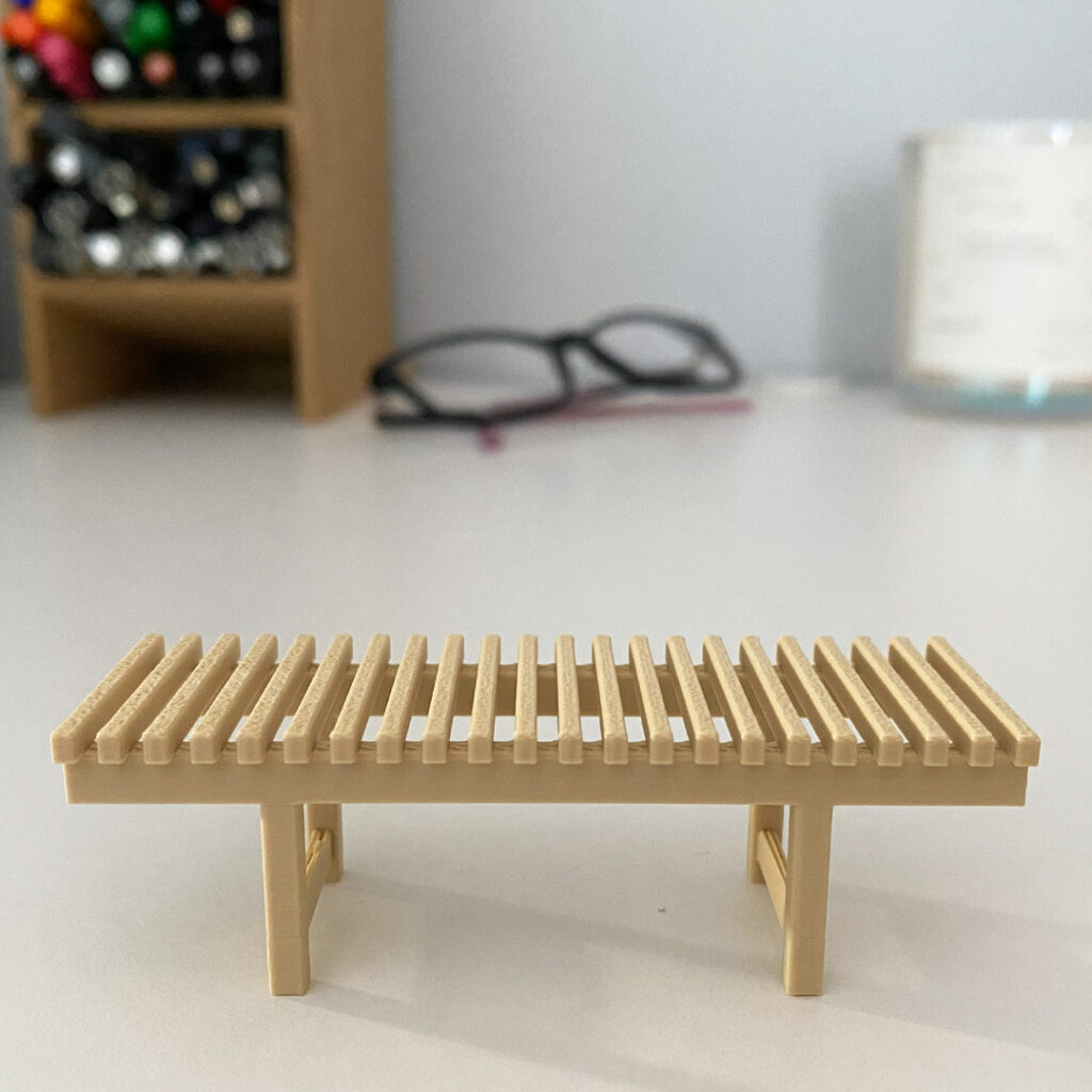 a photo of a tiny slated bench on a desk near some pens and a pair of glasses